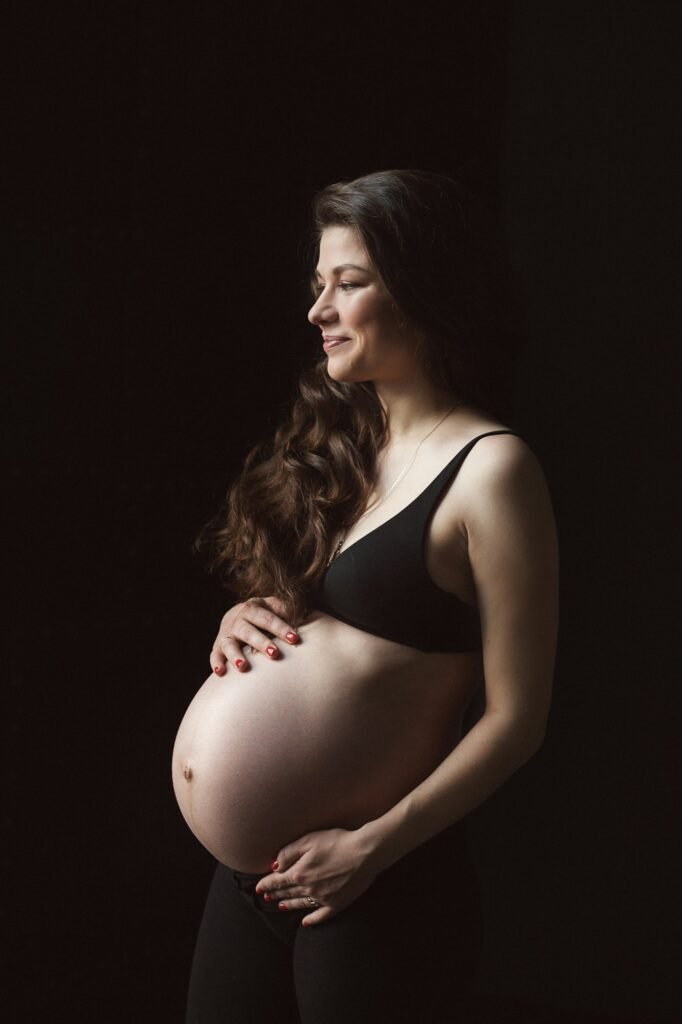 Young beautiful pregnancy woman in black lingerie with black background and long hair