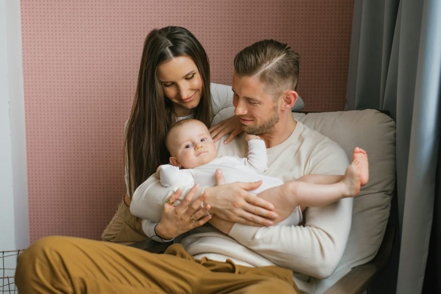 Young happy parents hold their baby son in their arms and smile looking at him